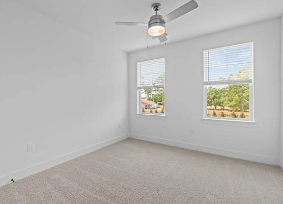 A room with a ceiling fan and two windows.