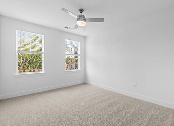 A room with a ceiling fan and two windows.