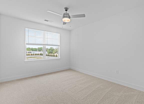 A room with a ceiling fan and a window showing trees outside.