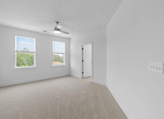 A room with a carpet floor, a ceiling fan, and a door.