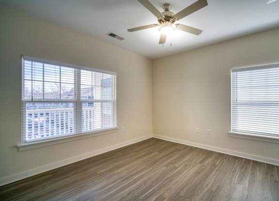 A room with a ceiling fan and two windows.
