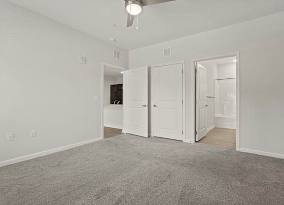 A room with a grey carpet and a ceiling fan.
