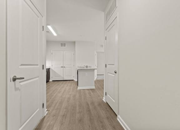 A white hallway with a door on the left and a kitchen area in the distance.