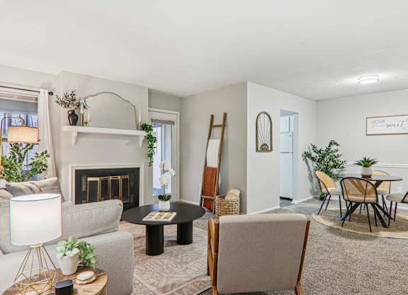 Plantations at Haywood staged living room with carpet, couch, ladder blanket, chairs and attached kitchen.