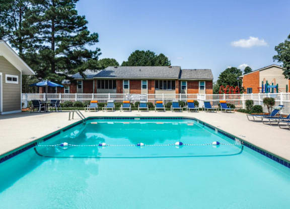 A swimming pool in front of a building with a white fence and trees.