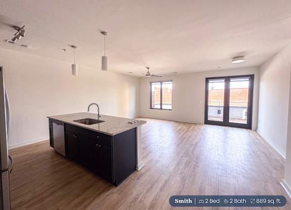 A spacious kitchen with a sink, refrigerator, and wooden flooring.
