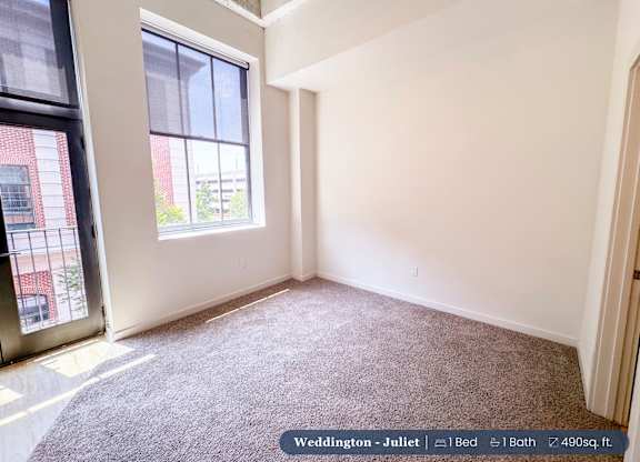 A bedroom with a large window and a carpeted floor.