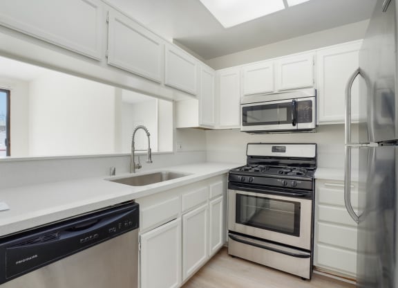 Apartment kitchen with stainless steel appliances, white counter tops and cabinets.
