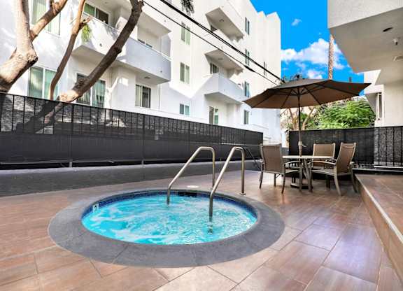 Spa in the middle of a patio with chairs and an umbrella at Park Rochester, Los Angeles, CA