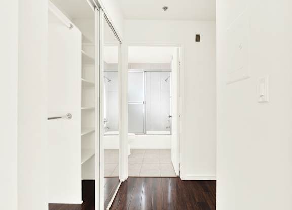A white hallway with a door on the left and a bathroom in the distance at Peach Tree Court, Los Angeles, 90024