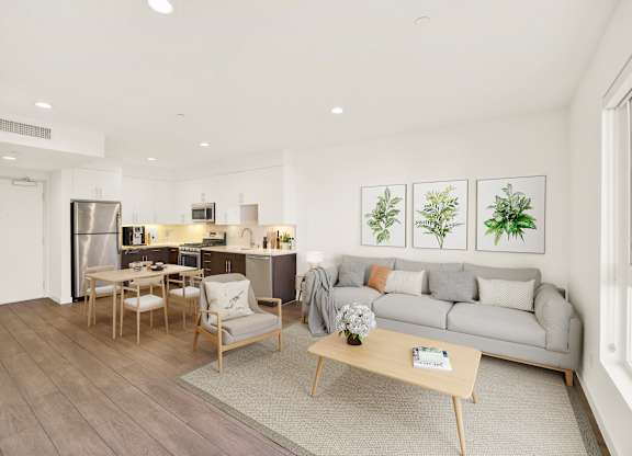 A modern living room with a grey sofa, wooden coffee table, and a kitchen area in the background at The Urbanpolitan, California 90036