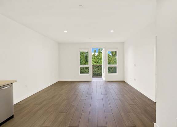 A large empty room with a dishwasher on the left and a window with a view of trees outside at The Urbanpolitan, Los Angeles, CA 90036