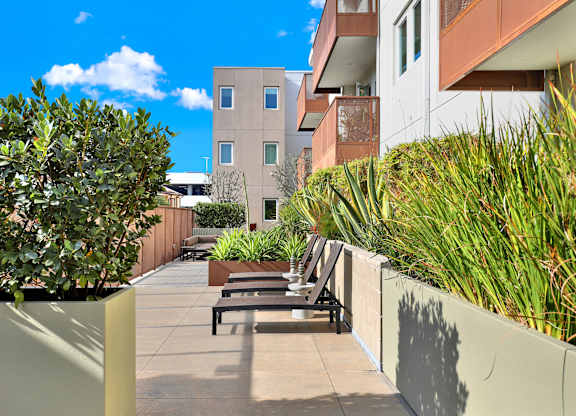 A sunny day in a courtyard with a bench and a building in the background at The Urbanpolitan, Los Angeles, CA 90036