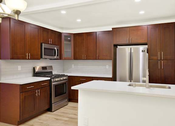 A kitchen with brown cabinets and a white counter at Wooster Encore Apartments, Los Angeles, CA 90035