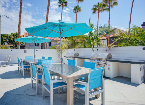 a patio with a grill and tables with blue chairs and umbrellas  at Laguna Gardens Apts., Laguna Niguel