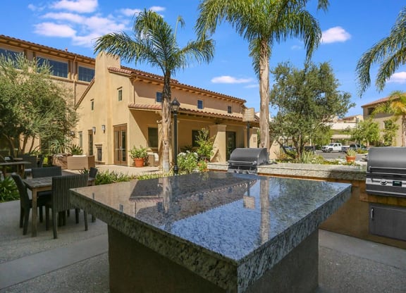 a patio with a table and chairs and a grill with palm trees in the background  at Ventana Senior Apartments, Northridge