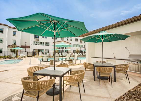A patio with a table and chairs under a green umbrella at Pradera Apartments, California, 94582