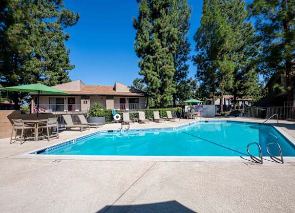 A swimming pool surrounded by trees and chairs.