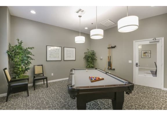 a game room with a pool table and two chairs  at Tesoro Senior Apartments, Porter Ranch, CA