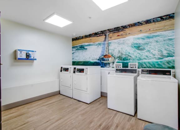 a laundry room with four washers and a painting of a beach on the wall at The Kenmore Los Feliz, Los Angeles, CA