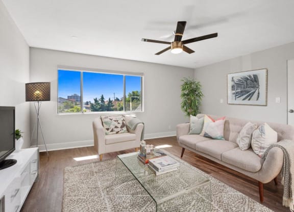 a living room with a ceiling fan and a large window at Palm Capri Apartments, California, 91501
