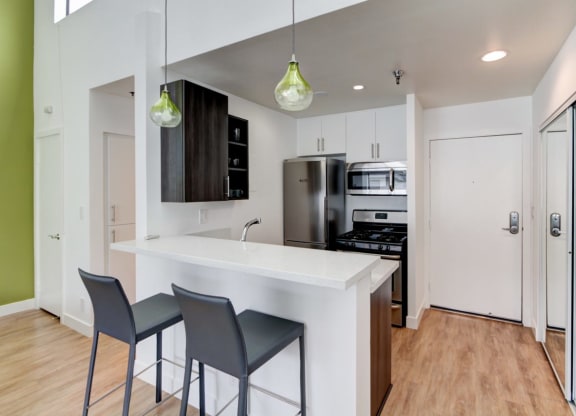 a kitchen with white cabinets and a white counter top with three stools in front of it  at El Greco Lofts, Los Angeles, CA, 90024
