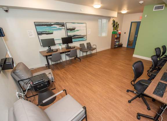 A room with a long table and chairs, a couch, and two computer monitors.