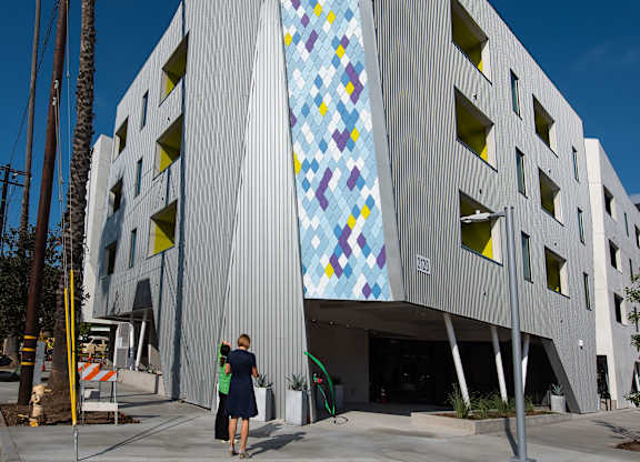 A woman stands in front of a building with a large mosaic on the side.