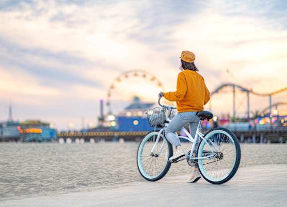 A person in a yellow jacket is riding a bicycle on a beach.