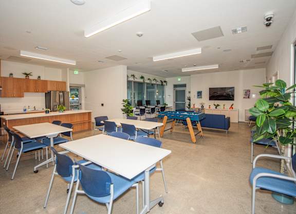 A room with tables and chairs and a kitchen area.