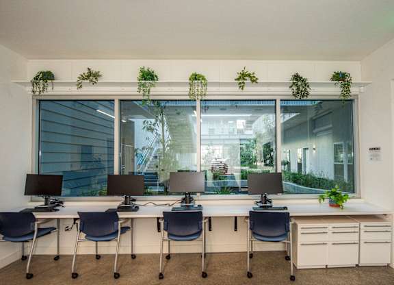 A white desk with four chairs and four monitors.