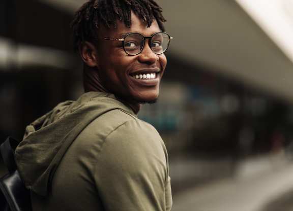 A man with dreadlocks and glasses is smiling.