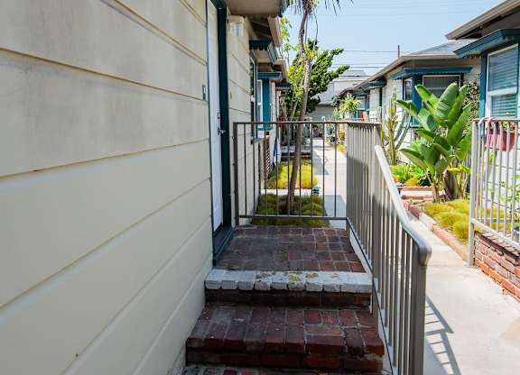 A small brick walkway leads to a door on a tan building.