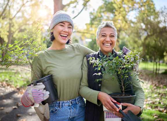 Two people holding potted plants in a garden.