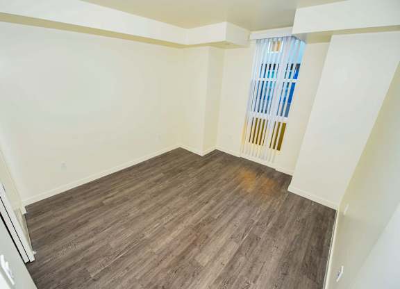 A room with wooden flooring and a window with a blue curtain.