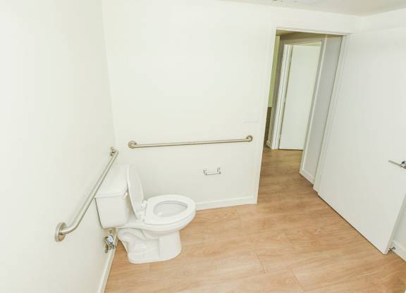Sample 2 Bed Unit: A white toilet with a silver grab bar is in a bathroom.