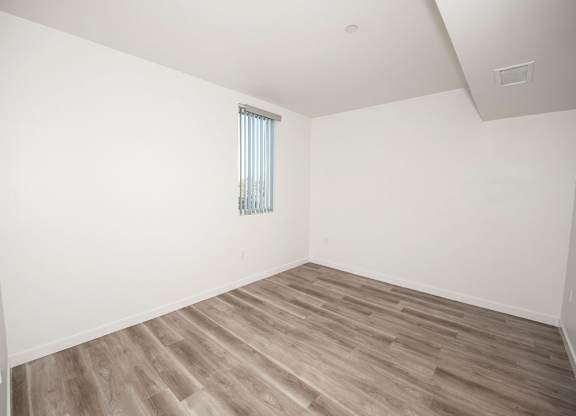 A room with wooden flooring and a window with blinds.