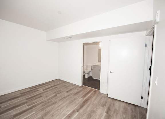 A room with a wooden floor and a toilet in the other room.