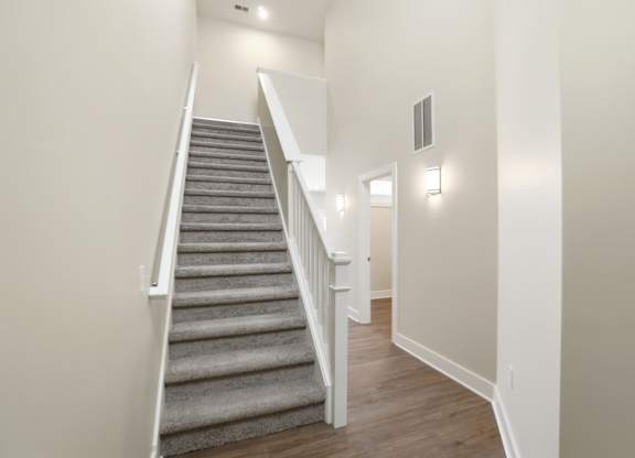 A staircase with a grey carpeted runner and white balusters.