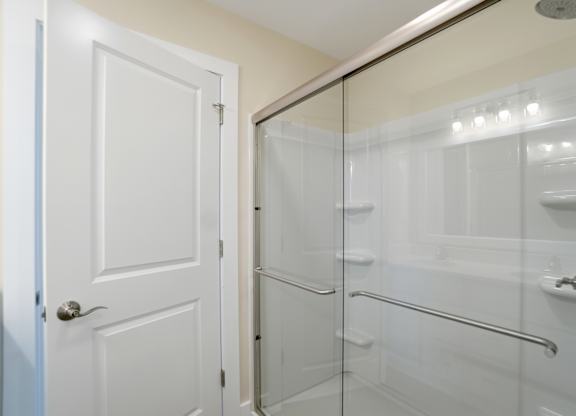 A white door is open to a bathroom with a glass shower stall.
