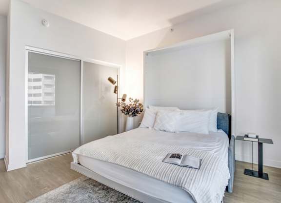 A bedroom with a large bed and a glass door leading to a balcony.at Wilshire Margot, Los Angeles, CA 90024 