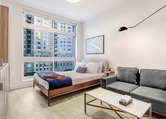 A bedroom with a bed, a couch, and a window overlooking a cityscape.at Wilshire Margot, California 