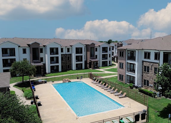 A swimming pool is surrounded by lounge chairs in a residential complex.
