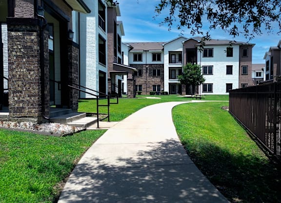 A long concrete walkway leads through a grassy area between two rows of apartment buildings.