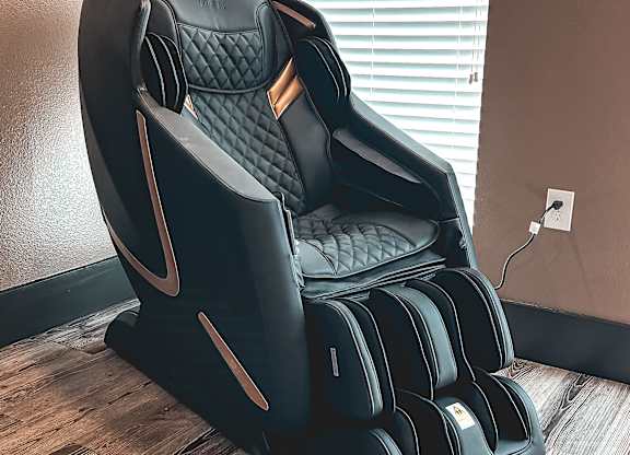 A black massage chair with a wooden base is placed in a room.