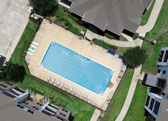 A swimming pool surrounded by a grassy area and apartment buildings.