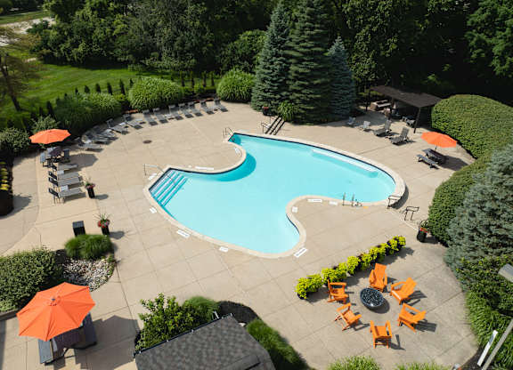 A large swimming pool surrounded by orange chairs and greenery.
