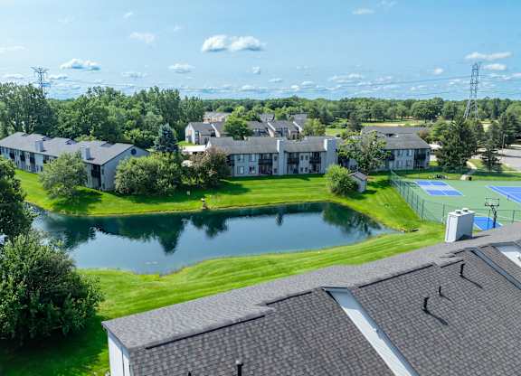 A large house with a pool is surrounded by other houses and trees.
