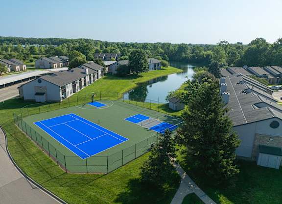 A tennis court surrounded by a fence and a pond in the background.