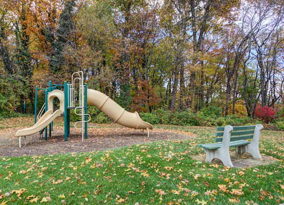 A playground with a yellow slide and two green benches at Highlands at Warwick Apartments, Pennsylvania 17543